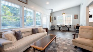 A living room with a sofa, coffee table, and armchair, large windows, and a ceiling fan.