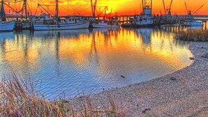 A harbor at sunset with boats docked, calm water, and a clear sky.