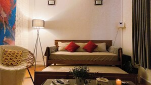 A bedroom with a bed, a chair, a bedside table, a lamp, and a painting on the wall. - Memories about Dalat in Indochine (Da Lat City)