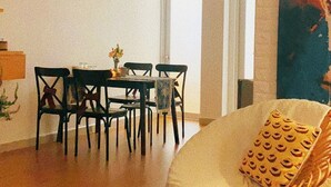 A spacious living area with a dining table and chairs, a sofa with a patterned cushion, and a bookshelf with books and a candle. - Memories about Dalat in Indochine (Da Lat City)