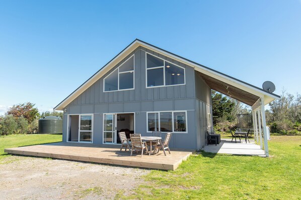 A two-story house with a covered patio, large windows, and a satellite dish. - Tokerau Magic - Karikari Peninsula Holiday Home (Kaitaia)