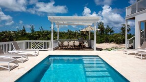 Ein klares, blaues Schwimmbecken mit einer Pergola und Sitzbereich im Freien, umgeben von Palmen und blauem Himmel.