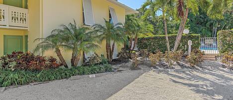 A yellow building with a balcony, palm trees, and a gravel pathway.