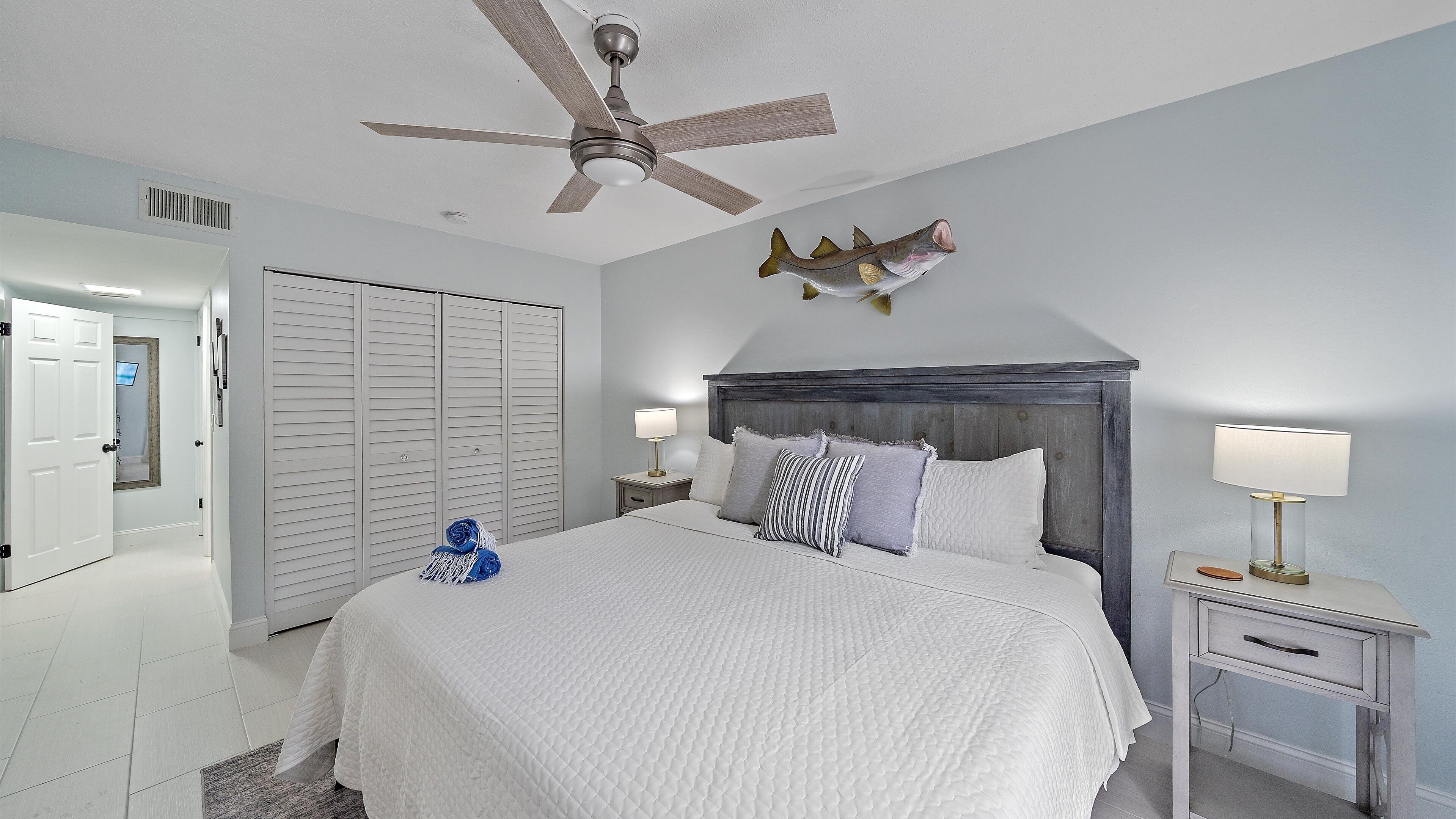 Une chambre à coucher avec un lit, une table de chevet, un ventilateur de plafond et un décor représentant des poissons sur le mur.
