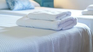 Una cama bien hecha con toallas blancas dobladas, un cabecero color turquesa, una lámpara de noche y un cuadro en la pared.