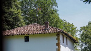Un edificio blanco con tejado de tejas, base de piedra y puerta azul. Hay sillas de metal dispuestas en semicírculo sobre el césped delantero.