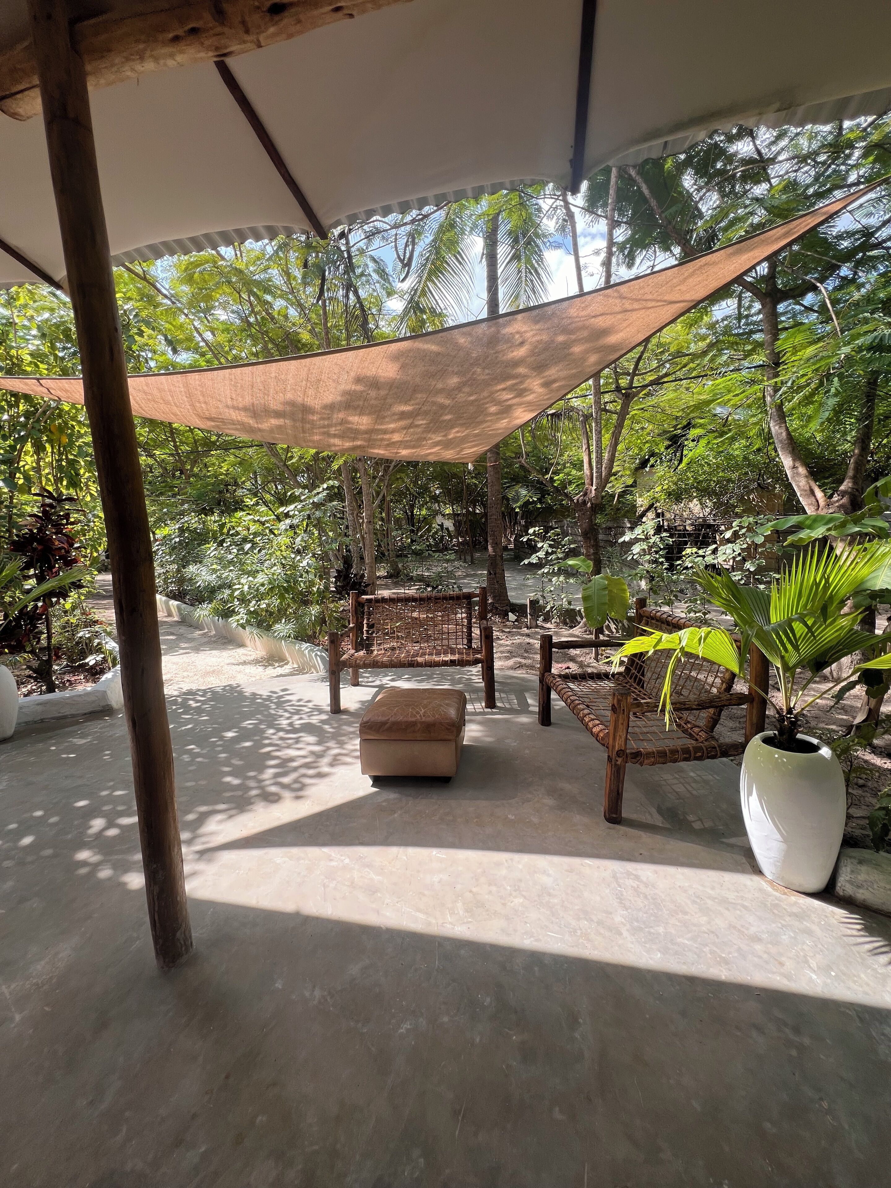 An outdoor seating area with a shaded canopy, wooden furniture, and potted plants.