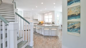 Eine moderne Küche mit weißen Schränken, einer zentralen Kochinsel mit Barhocker und einer Treppe mit Glastrennläufern.