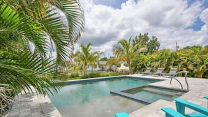 Ein Swimmingpool mit gefliestem Deck, umgeben von Palmen und Liegestühlen.