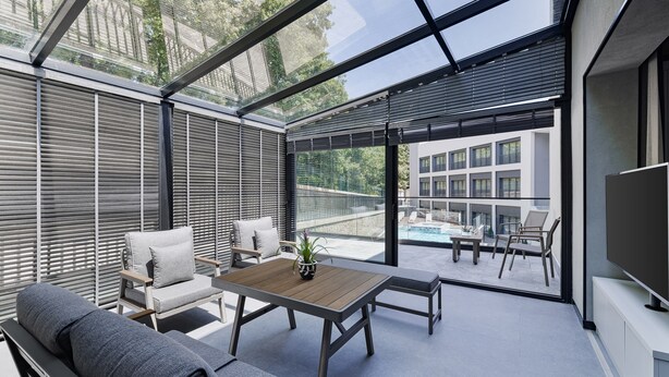 A modern outdoor living space with a glass enclosure, a wooden table, and seating. - INVENTIST Hotel Sports Academy (Çekmeköy)