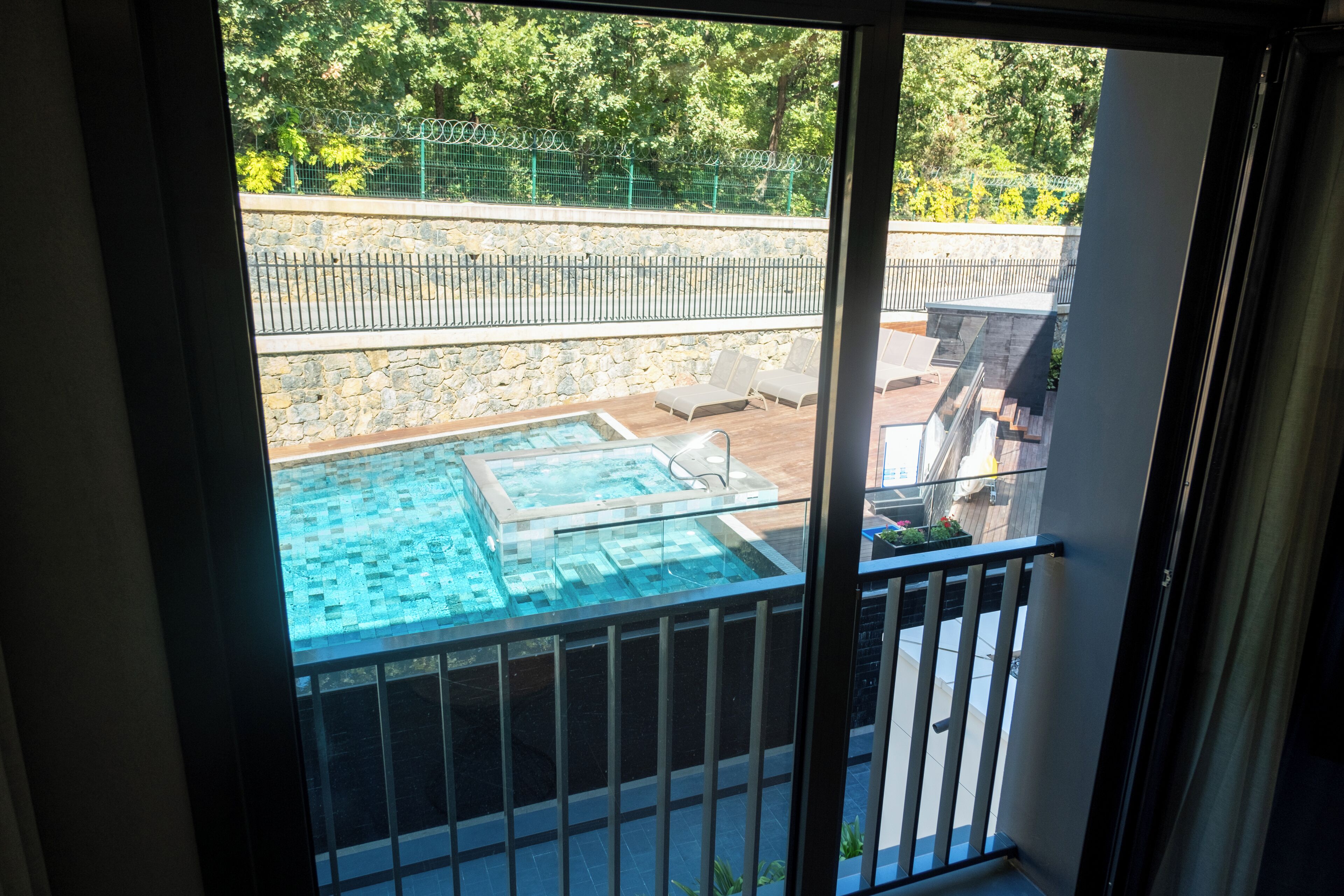 A glass-enclosed balcony with a view of a swimming pool and lounge chairs.