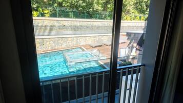A glass-enclosed balcony with a view of a swimming pool and lounge chairs.