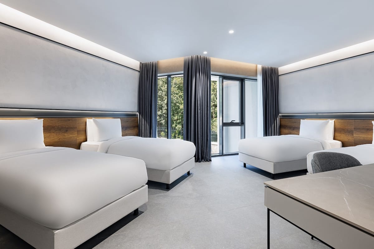 Ein modernes Hotelzimmer mit zwei Betten, einem Schreibtisch und großen Fenstern mit Vorhängen.