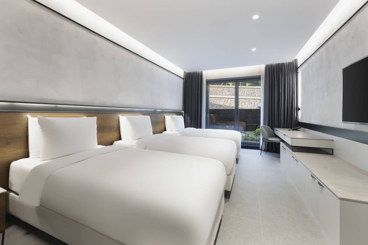Ein modernes Hotelzimmer mit zwei Betten, einem Schreibtisch und einem großen Fenster mit Vorhängen.