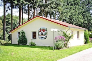 A single-story building with a red roof, a small porch, and a circular mural on the front wall.