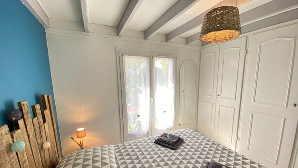 Une chambre à coucher comprenant un lit, une table de chevet, une lampe, une fenêtre avec des rideaux et une armoire.