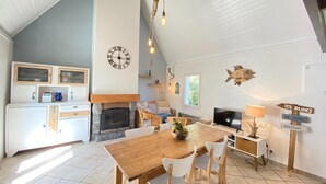 Un vaste espace de vie doté d’une cheminée, d’une table à manger en bois et d’un téléviseur.