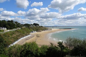 Une plage côtière avec un rivage rocheux, une promenade et des maisons situées sur une colline.