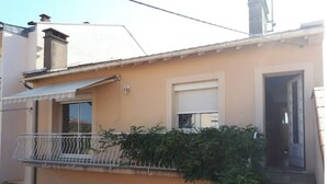 Un bâtiment à deux étages doté d’un balcon, d’une fenêtre avec un volet et d’une porte donnant sur un escalier.