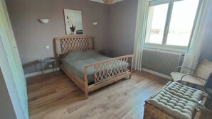 Une chambre à coucher avec un lit en bois, une petite table ronde, une chaise et un radiateur.