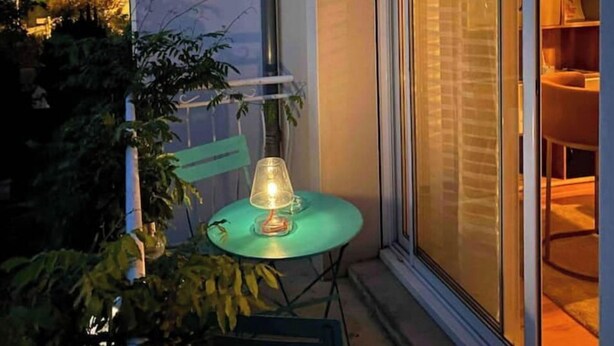 Un balcon avec une table et des chaises, un luminaire suspendu et une porte-fenêtre coulissante donnant sur un espace intérieur.
