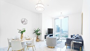 Un soggiorno moderno con zona pranzo, un divano grigio, una televisione e un'ampia finestra con vista sulla città.