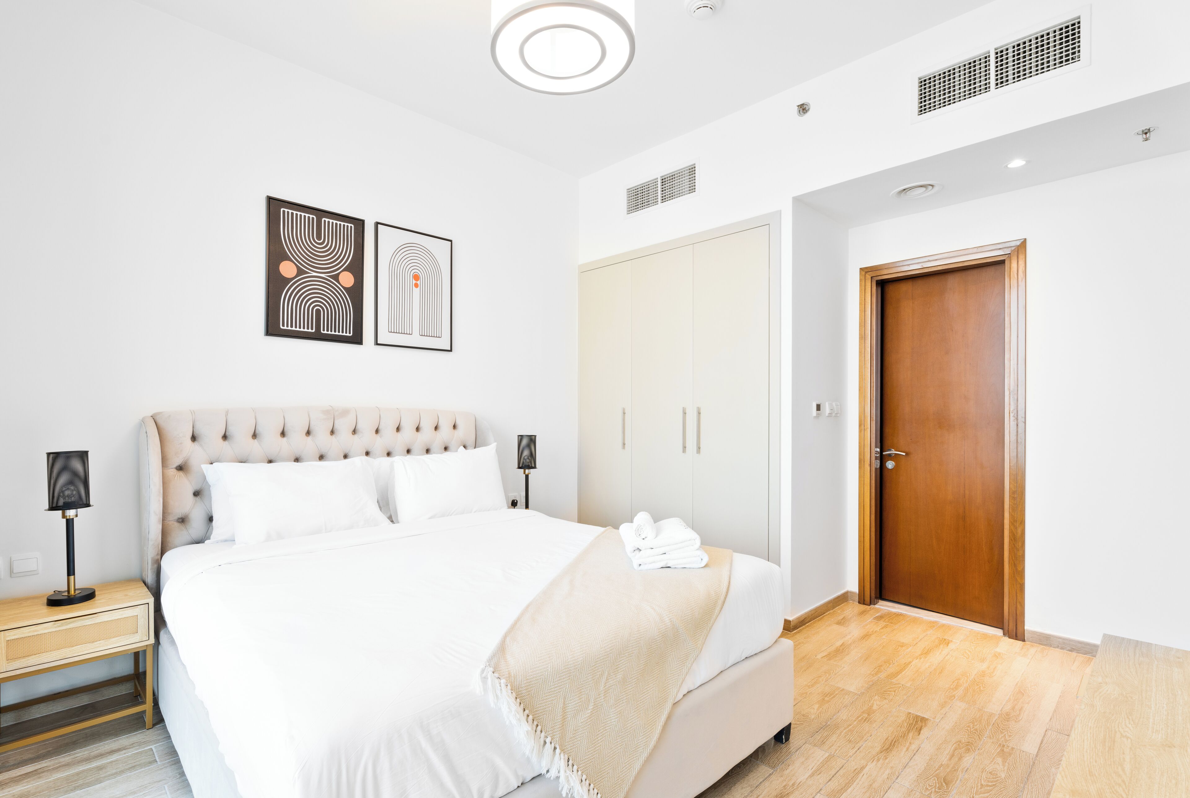 Un dormitorio ordenado con una cama grande, lámparas de noche, un armario y una puerta.