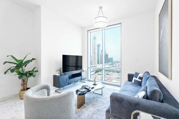 A modern living room with a large window, a flat-screen TV, a grey sofa, and a coffee table.