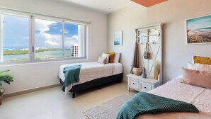 Ein Schlafzimmer mit zwei Betten, einem großen Fenster mit Meerblick, einer Decke mit orangen Paneelen und einem Nachttisch mit einer Lampe.