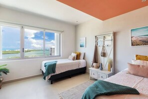 Enjoy a serene coastal view from the large window in this stylish bedroom featuring two beds and a wardrobe with mirror.