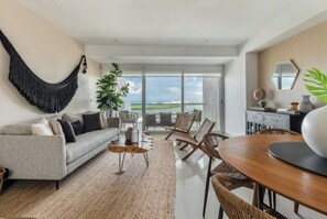 Relax in this stylish living room with a large sofa, coffee table, and dining area, offering a view of the outdoors.