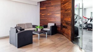 Ein moderner Innenraum mit einer Holzvertäfelung, einer Sitzecke mit zwei Sofas und einem Tisch sowie einer Glastür zum Fitnessbereich.