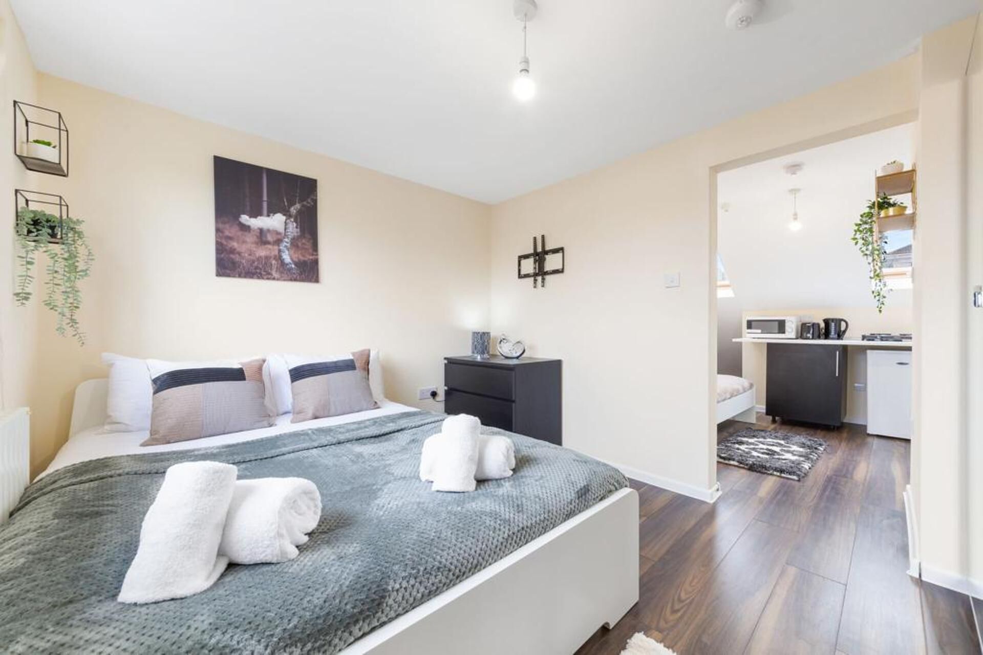 A modern bedroom with a bed, bedside tables, a desk, and a kitchen area.