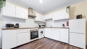 A modern kitchen with white cabinets, a wooden countertop, a built-in oven, a microwave, a washing machine, and a fire extinguisher. - Remarkable 2 Double Bed Ensuite Room Isleworth TW7 (Isleworth)
