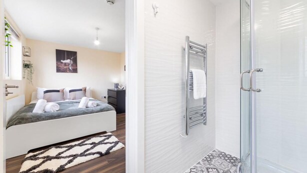 A modern bedroom with a bed, bedside table, and a large window. - Remarkable 2 Double Bed Ensuite Room Isleworth TW7 (Isleworth)