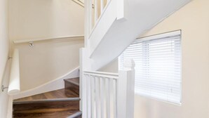 A staircase with wooden steps and white railings, leading to a landing with a window with blinds. - Remarkable 2 Double Bed Ensuite Room Isleworth TW7 (Isleworth)