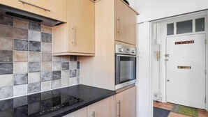 A kitchen with light wooden cabinets, a black countertop, and a tiled backsplash. - Duplex 3 Bedroom Flat Golders Green Central London (London)