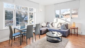 A modern living room with a sofa, chairs, a coffee table, and large windows providing natural light. - Duplex 3 Bedroom Flat Golders Green Central London (London)