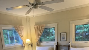 A bedroom with two white beds, a ceiling fan, and windows with curtains.