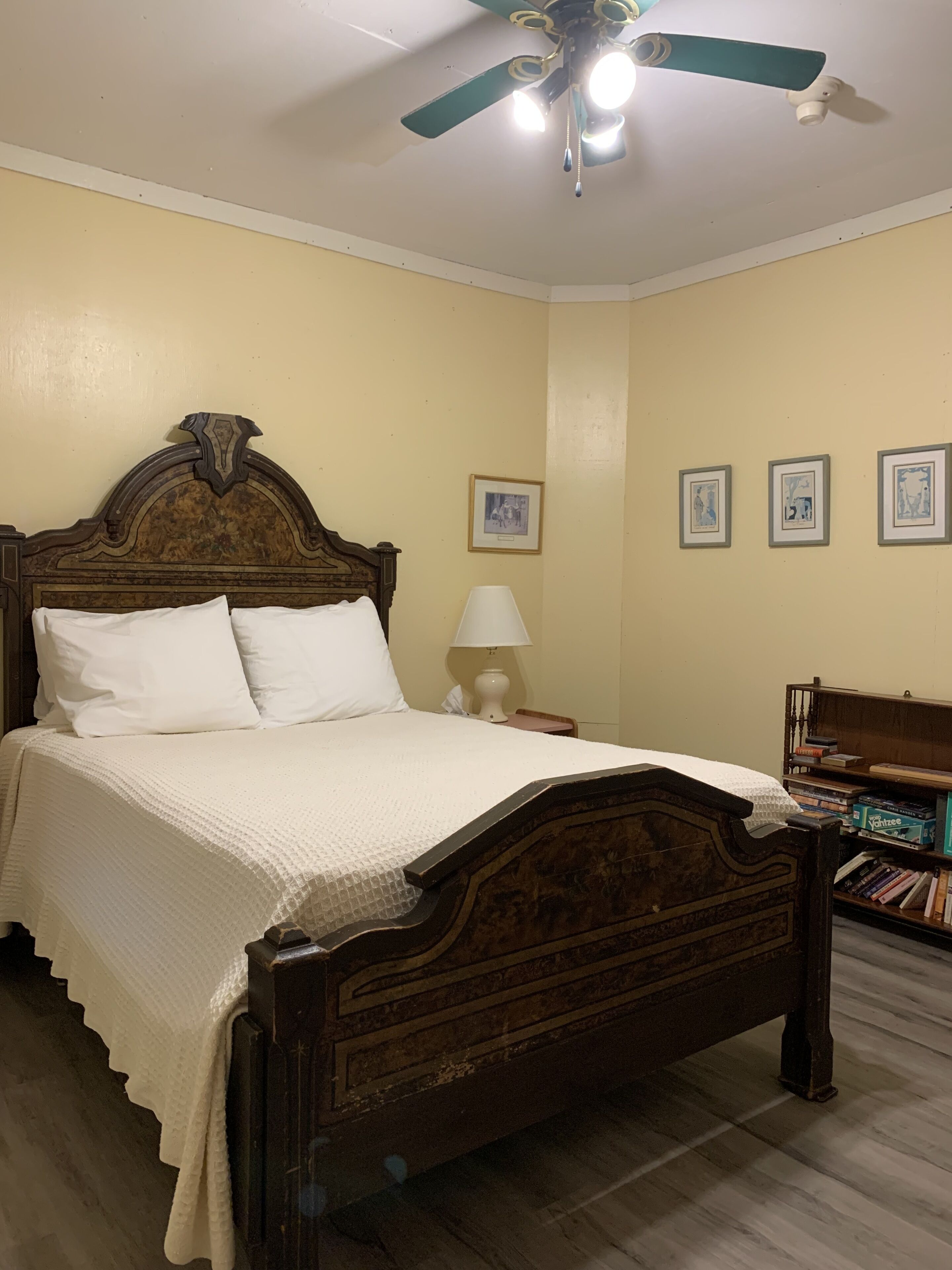 A bedroom with a wooden bed, a ceiling fan, a bedside lamp, and a bookshelf.