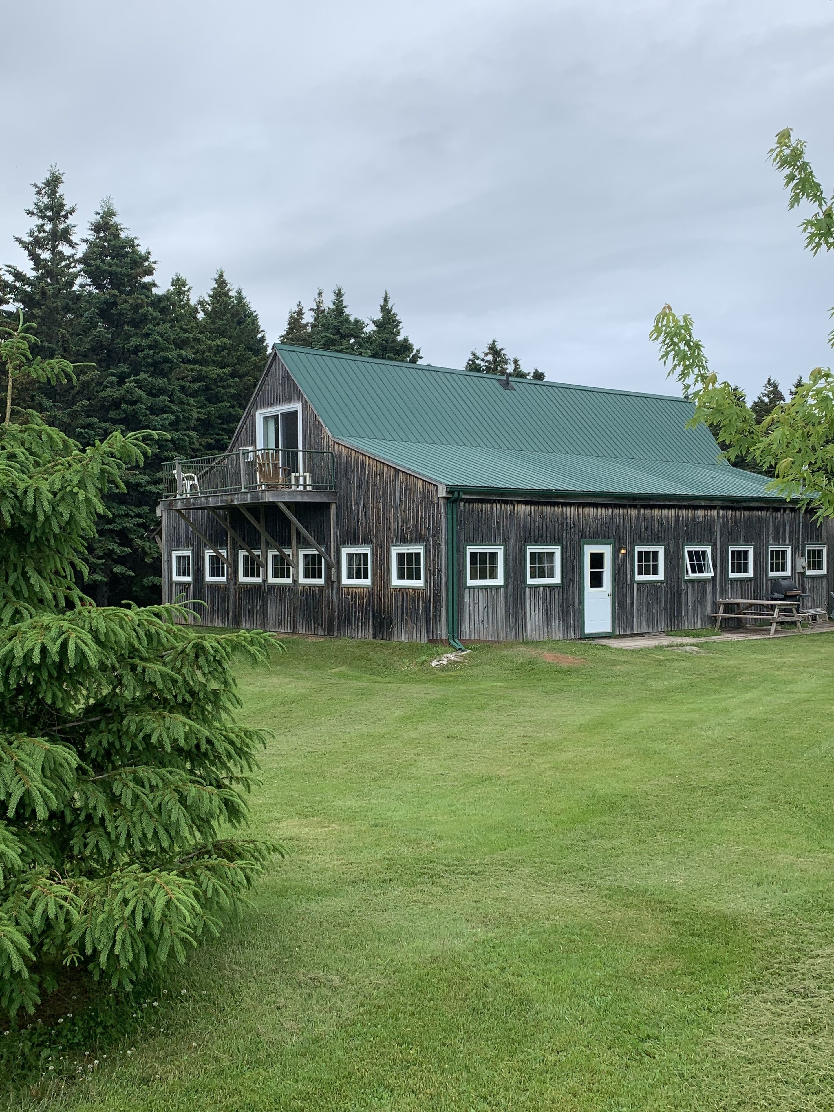 A rustic wooden barn with a green roof, surrounded by lush greenery and trees.