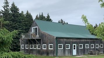 A rustic wooden barn with a green roof, surrounded by lush greenery and trees.
