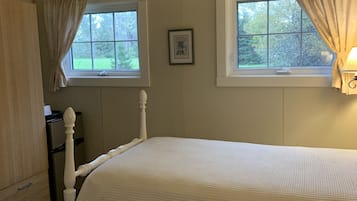 A bedroom with two beds, a ceiling fan, a window with curtains, and a framed picture on the wall.