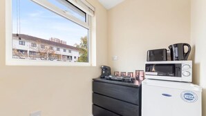 A compact kitchenette with a microwave, coffee maker, and small refrigerator. A window offers a view of a building outside.