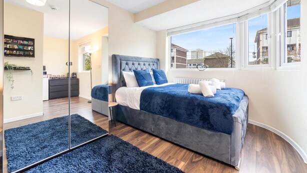 A modern bedroom with a large bed, a walk-in closet, and a view of the city through large windows.
