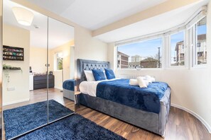A modern bedroom with a large bed, a walk-in closet, and a view of the city through large windows. - Spacious Sleeps 3 Ensuite Room In Twickenham TW7 (Isleworth)