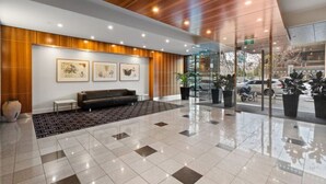 A modern lobby with a wooden ceiling, a black leather sofa, a tiled floor, and framed artwork on the wall. - Central 2BR Apt in Southbank (Southbank)