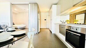 A modern kitchen with a dining area, stainless steel appliances, and a view into the adjacent bedroom.