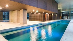 An indoor swimming pool with a modern design, surrounded by tiled walls and a high ceiling.