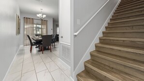 Eine Treppe mit Holzstufen und einem weißen Geländer, die zu einem Raum mit Essbereich, Tisch und Stühlen führt.